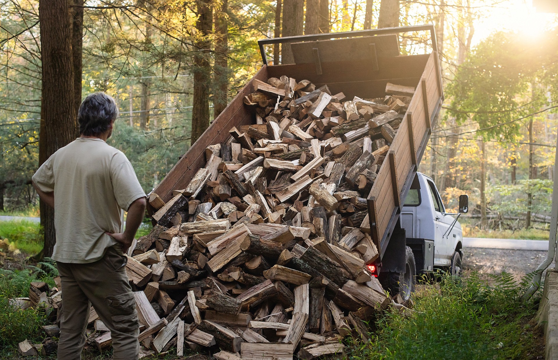 Firewood delivery in Poconos. 53 years old man watching as firewood spills from a truck onto a driveway, rural Pennsylvania setting